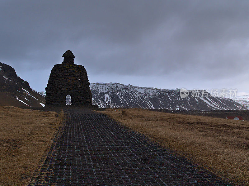 观火山岩石的一个大雕像与Bárðar saga Snæfellsáss在小村庄阿纳斯塔皮在冬天与山。